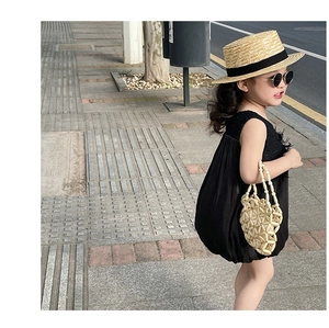 Detail of a child in a black bubble hem dress with a beige beaded handbag outdoors