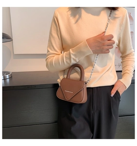 Detail einer braunen Umhängetasche aus Leder mit Kette, getragen von einem Model zu Hause