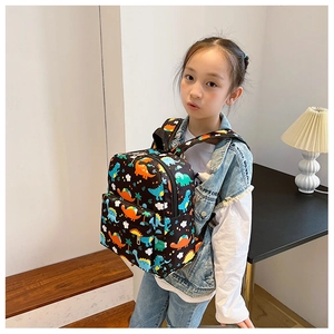 Detail of child wearing a black backpack with colorful cartoon dinosaur prints in a room