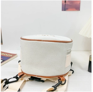 Détail du bas du petit sac à dos en toile avec garniture en cuir brun et sangle blanche