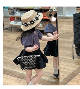 Close-up of a child's black geometric woven bead handbag with floral straw hat accessory