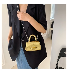 Detail of a mini metallic gold handbag featuring a structured handle and beaded chain strap