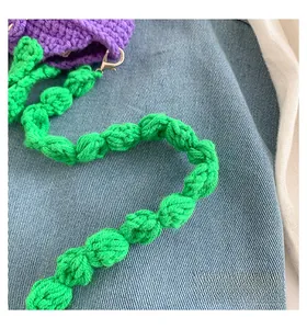 Detail of green bubble-knit strap and purple crochet bag with metal lobster clasp