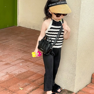 Outfit alla moda da bambina con top a righe, pantaloni neri e mini borsa a tracolla a conchiglia