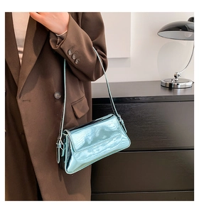 Metallisch blaue Schultertasche mit glänzender Lackleder-Optik an einer Schulter getragen