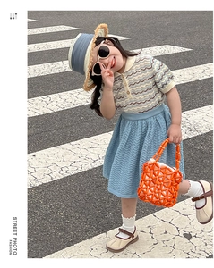 Close-up of bright orange woven handbag with blue pleated skirt and polo shirt for girls