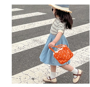 Detail of girls knit outfit with blue pleated skirt and orange woven bead handbag