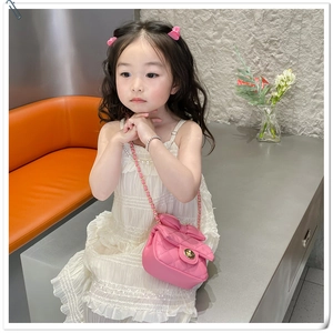 Pink quilted mini crossbody bag with bow and gold clasp worn by a young girl