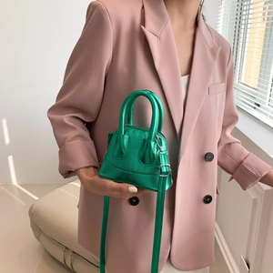 Mini shell bag in metallic green crocodile texture shown on a pink blazer