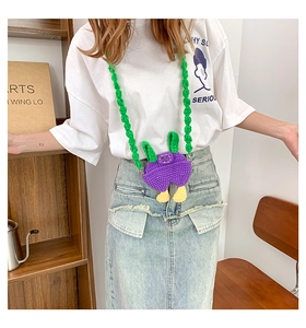 Close-up of handmade purple knitted overall-shaped mini bag with green woven strap