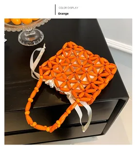 Detail of orange beaded handmade bag with white silk ribbon handle on black surface