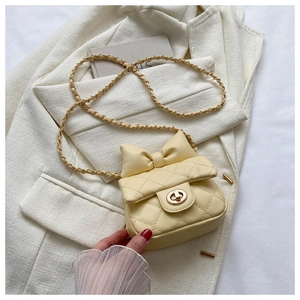 Close-up of yellow quilted crossbody bag with bow detail and gold chain strap on blazer