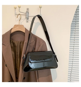 Detail einer glänzenden schwarzen Lackledertasche kombiniert mit einem braunen Sakko