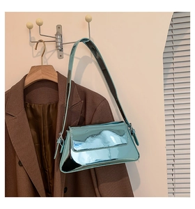 Detail einer blauen glänzenden Lackleder-Schultertasche hängend vor braunem Blazer