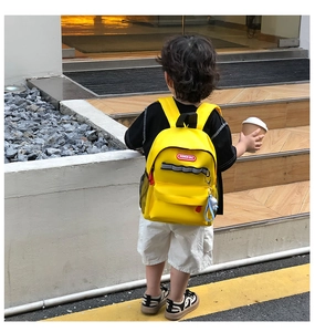 Rear view of a yellow canvas kids backpack with a blue plush charm in outdoor sunlight