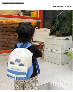 Blue and white children's backpack with Keep Smiling embroidery shown in a street setting