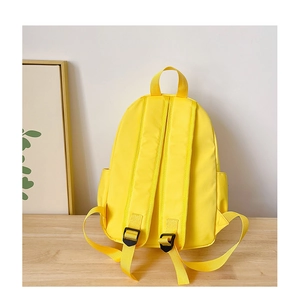 Detail view of yellow school bag with padded shoulder straps and side pockets on wooden table