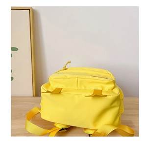 Detail view of a bright yellow kids backpack on a wooden table with a white background
