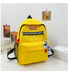 Detail of yellow canvas backpack with front zipper pocket and blue astronaut pendant