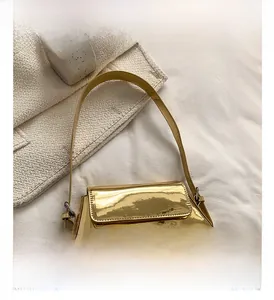 Makro-Detail der glänzend goldenen Baguette-Tasche mit Umschlagklappe auf weißem Stoff