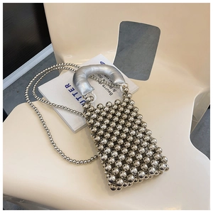Dettaglio di una borsa a mano con perle argentate su una sedia bianca con rivista d'arte
