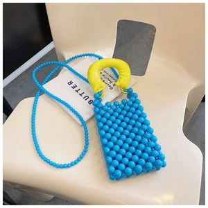 Borsa a tracolla in perline blu con manico giallo a contrasto appoggiata su una sedia