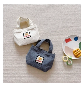 Detail of mini corduroy tote bags with cute cartoon bear patches in cream and navy blue