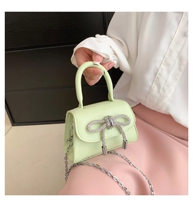 Close-up of mint green mini handbag featuring a rhinestone bow and silver chain strap