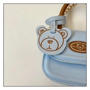 Detail of light blue mini bag featuring brown handle, bear charm, and golden chain