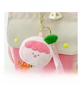 Close-up of a pink peach plush charm with a gold keyring on a canvas backpack