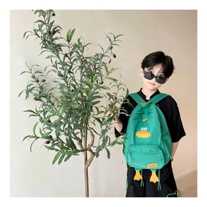 Detail view of the green cartoon duck backpack worn by a toddler in an outdoor setting
