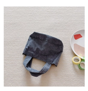 Flat lay of dark grey corduroy handbag with minimalist ceramic decor on textured rug
