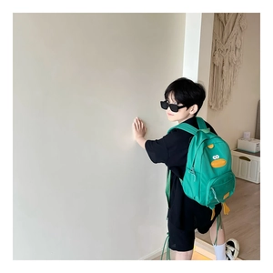Toddler wearing green cartoon duck backpack with yellow beak and feet details