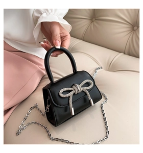 Detail of black mini handbag featuring a diamond bow ornament and silver chain strap