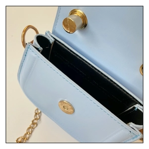Detail view of mini blue chain bag featuring golden magnetic snap and black inner lining