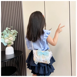Detail van rieten crossbodytas voor kinderen met lichtblauwe kanten strik en parelaccenten