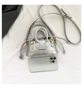 Silver mini handbag with gold hardware and phone for size reference on white cloth