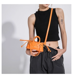 Detail of bright orange mini handbag with cylindrical handle and drawstring closure