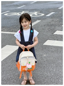 Outdoor shot of a kids color-block canvas backpack with cute peach plush charm