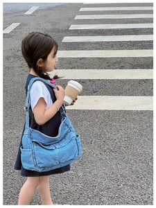 Detail of blue denim kids crossbody bag with functional exterior pockets and wide strap