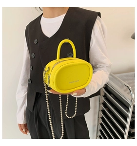 Detail of yellow pebbled leather mini bag with pearl chain strap and handle shown on model
