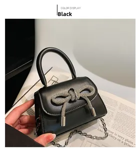 Detail of a black mini handbag featuring a sparkling rhinestone bow and silver chain strap