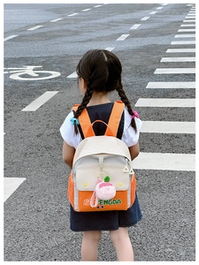 Outdoor shot of kids canvas backpack in orange and white with a pink peach plush charm