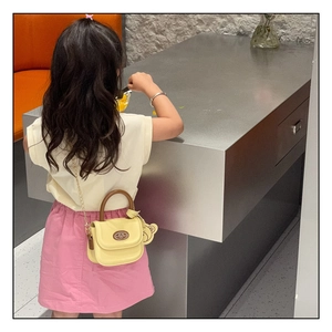 Close-up of yellow PU leather girls bag with bear charm and golden chain strap