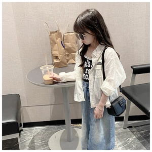 Girl wearing a white sheer shirt, black printed vest, and denim skirt with a black crossbody bag