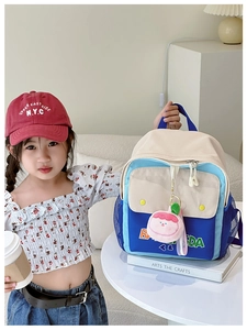 Close-up of color-block kids canvas backpack with peach plush charm and letter detail