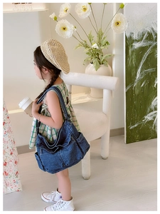 Detail view of large dark blue denim crossbody bag with side pockets on a child model