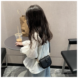 Close-up of a child wearing a black faux leather mini crossbody bag in a cafe setting