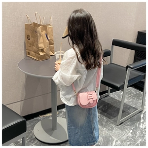 Pink girls mini saddle bag in lychee pattern PU leather worn in a cafe setting