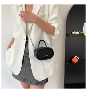Mini black pebble leather oval bag with silver chain worn by model in white suit